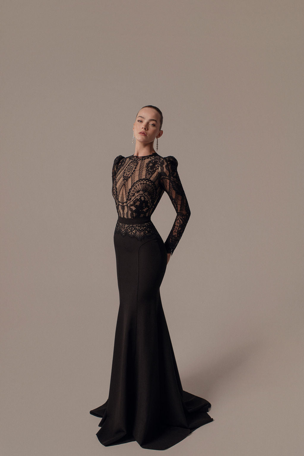 אישה פוזלת בחינניות בשמלת Leya מקולקציית ערב 2026, עם פרטים מתחרה שקופה על המחוך והשרוולים. שיערה מסורק לאחור, והיא עומדת על רקע ניטרלי ופשוט.