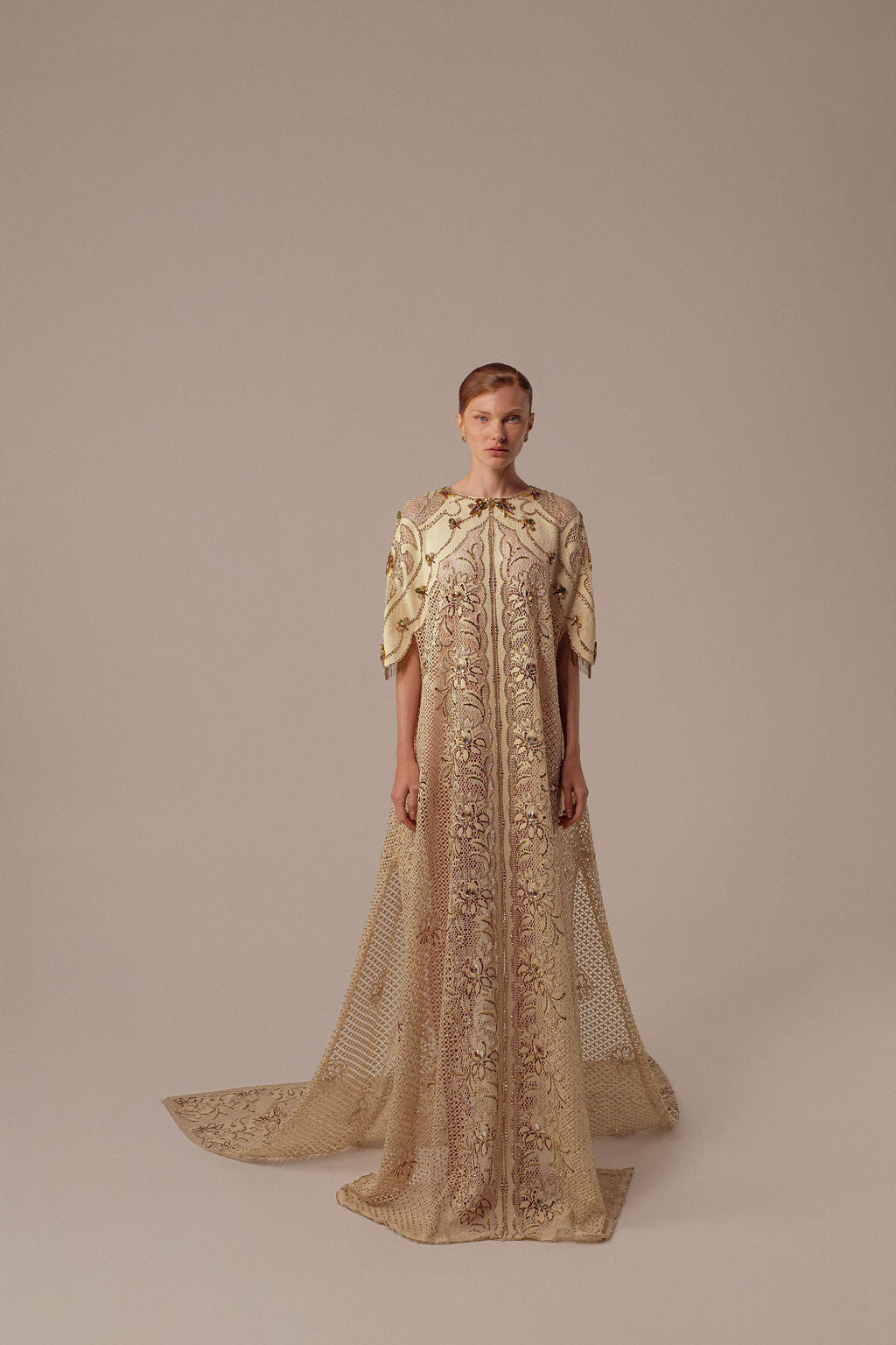 אדם בעל עור בהיר ושיער חום קצר לובש את שמלת Mira מקולקציית הערב 2026 של דרור קונטנטו — שמלת ערב מעוטרת בצבעי שמנת וזהב עם רקמת פרחים מורכבת — על רקע ניטרלי.