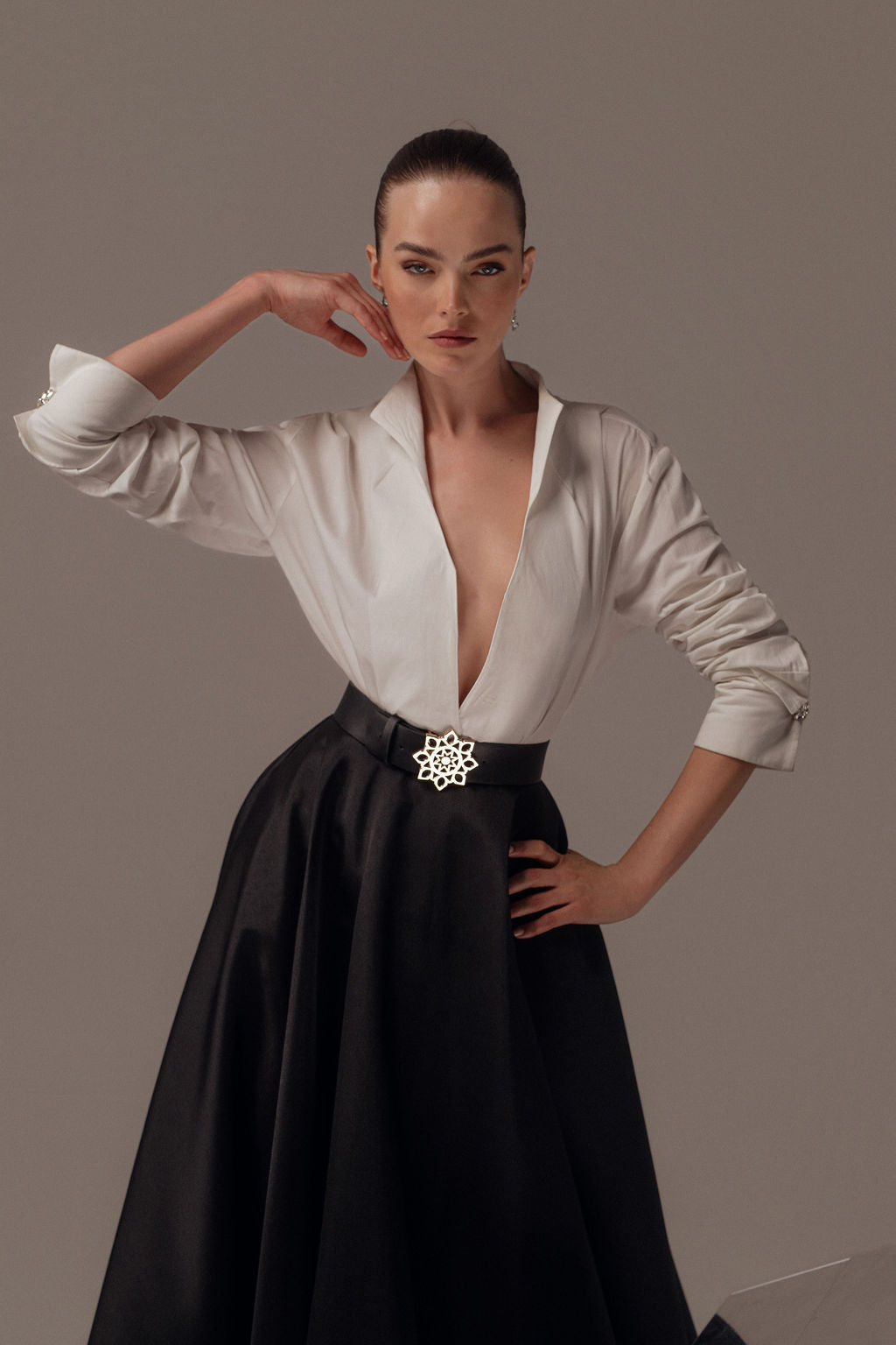 אישה מצטלמת בביטחון בשמלת Elyn מקולקציית הערב 2026 של דרור קונטנטו, עם מחשוף עמוק וחצאית שחורה ארוכה. שיערה מסורק לאחור והיא עומדת על רקע ניטרלי ורגיל.