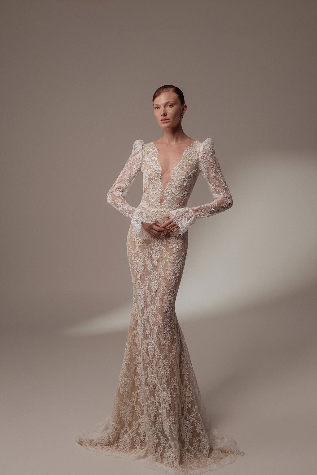 אישה מדגמנת שמלת ערב ארוכה ומחמיאה מקולקציית Zara - Dress | Evening 2026, עם תחרה שקופה, מחשוף עמוק, דוגמאות פרחוניות מורכבות ושובל עדין על רקע ניטרלי.