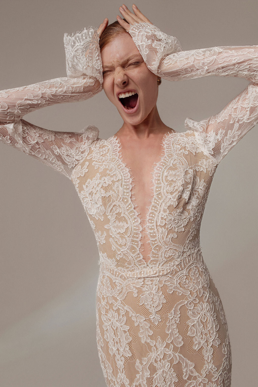 אדם לבוש בשמלת תחרה ארוכת שרוולים מקולקציית Zara - Dress | Evening 2026, עומד עם ידיו על הראש, עיניים עצומות ופה פתוח, בתסכול או התרגשות ניכרים, על רקע ניטרלי.