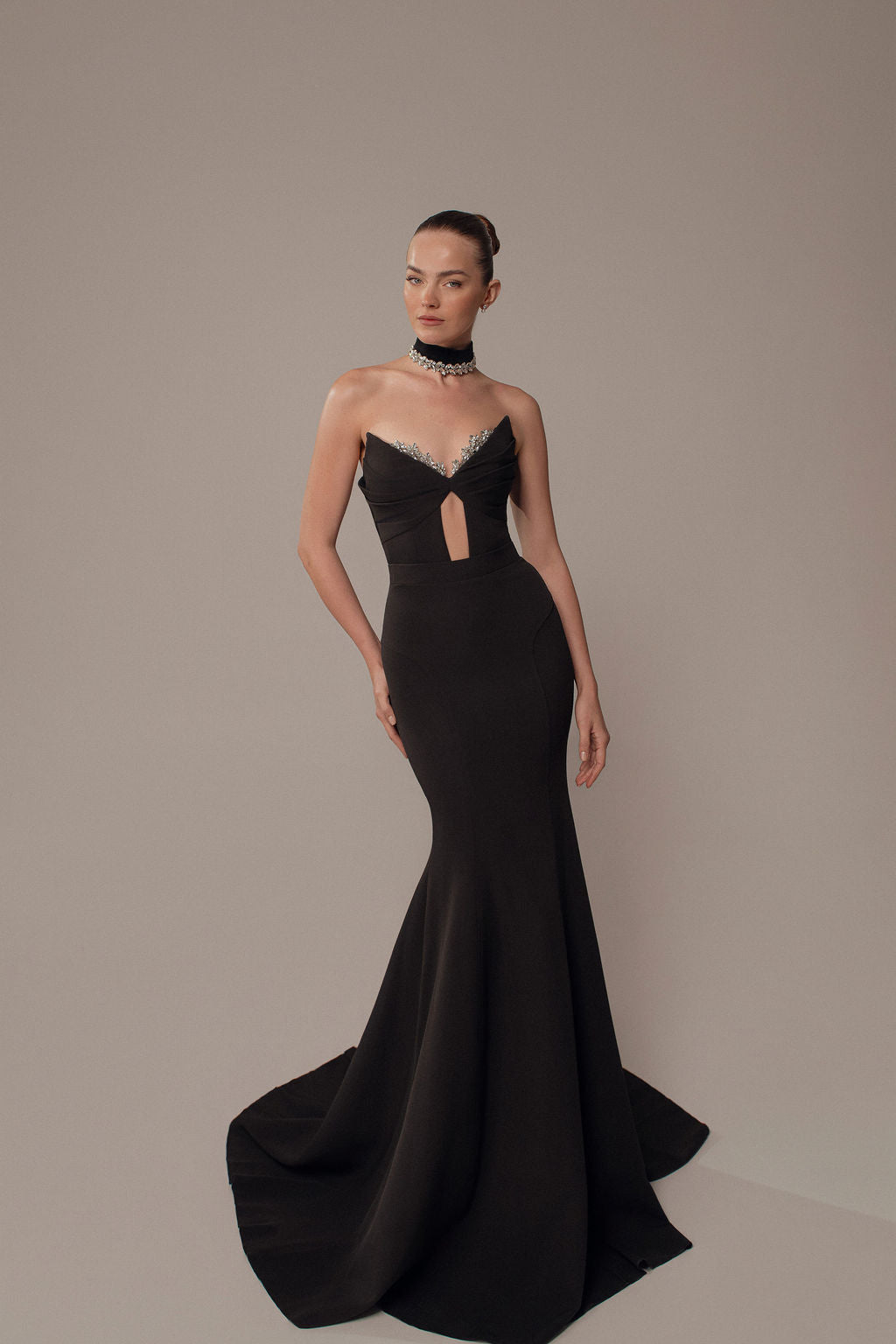 אישה לובשת את שמלת Maya מקולקציית ערב 2026 של דרור קונטנטו — שמלת ערב שחורה צמודה באורך הרצפה עם גזרת בת ים, מחשוף מפתח בחזה, צווארון נוצות, שיער אסוף לאחור ושרשרת קולר משובצת אבנים.