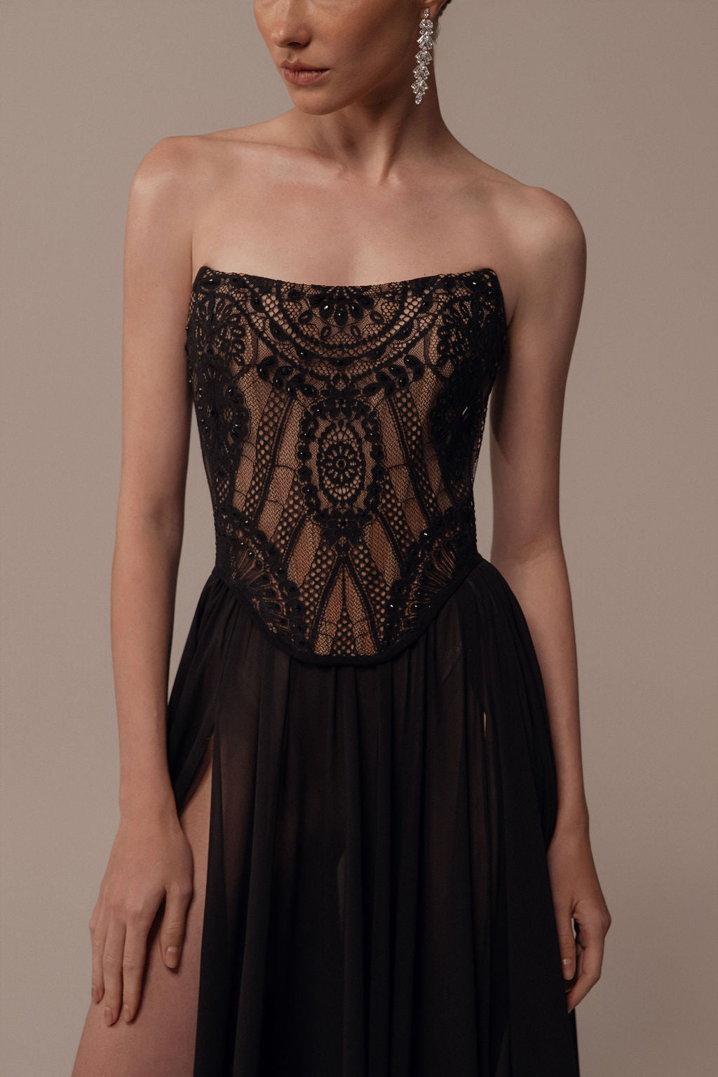 אישה לובשת את שמלת Alma מקולקציית ערב 2026 של דרור קונטנטו, עם מחוך תחרה שחור ללא כתפיות וחצאית שקופה וזורמת. היא מצטלמת עם עגילים תלויים, פניה חלקית מחוץ לפריים — אידיאלי לכל אירוע שמלת ערב.