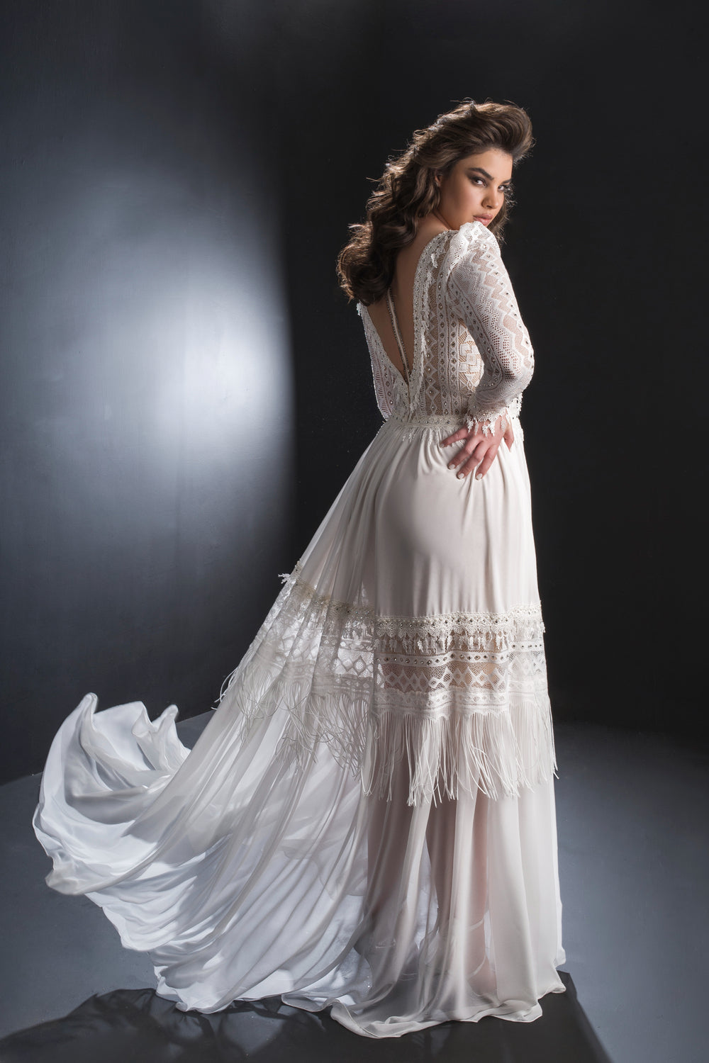 אישה מדגמנת את שמלת איזבלה מקולקציית Bridal Plus 2019 של דרור קונטנטו, עומדת בסטודיו מואר באור עמום ומשדרת אלגנטיות בשמלת כלה ארוכה, לבנה ועשויה תחרה.