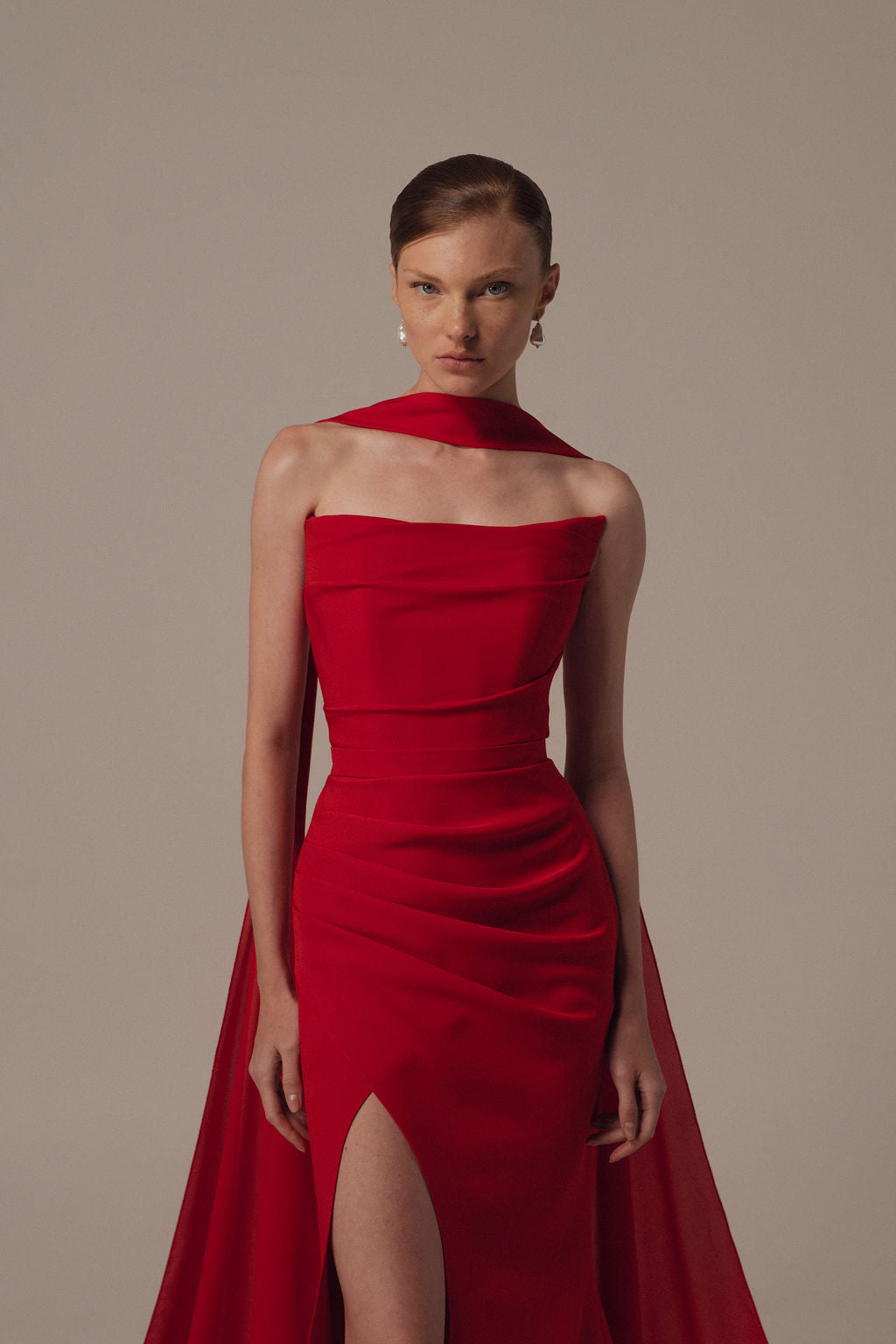 אישה בעלת עור בהיר ושיער חום אסוף לאחור מצטלמת ברצינות על רקע אחיד, לבושה בשמלה האלגנטית "Miri - Dress" מקולקציית ערב 2026, עם חתך גבוה ופרט תואם על הכתפיים.