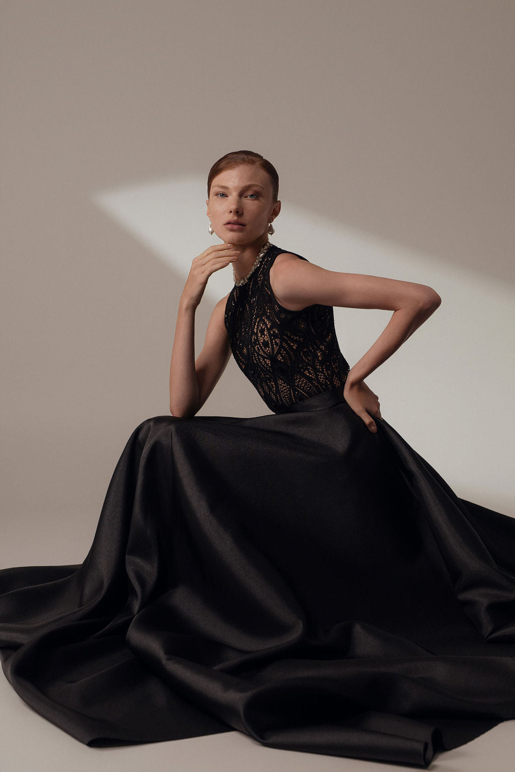 אישה עם שיער קצר מצטלמת באלגנטיות בשמלת Lia מקולקציית Evening 2026, עם מחוך תחרה וחצאית מתנפנפת ונפוחה, על רקע ניטרלי בתאורה רכה.