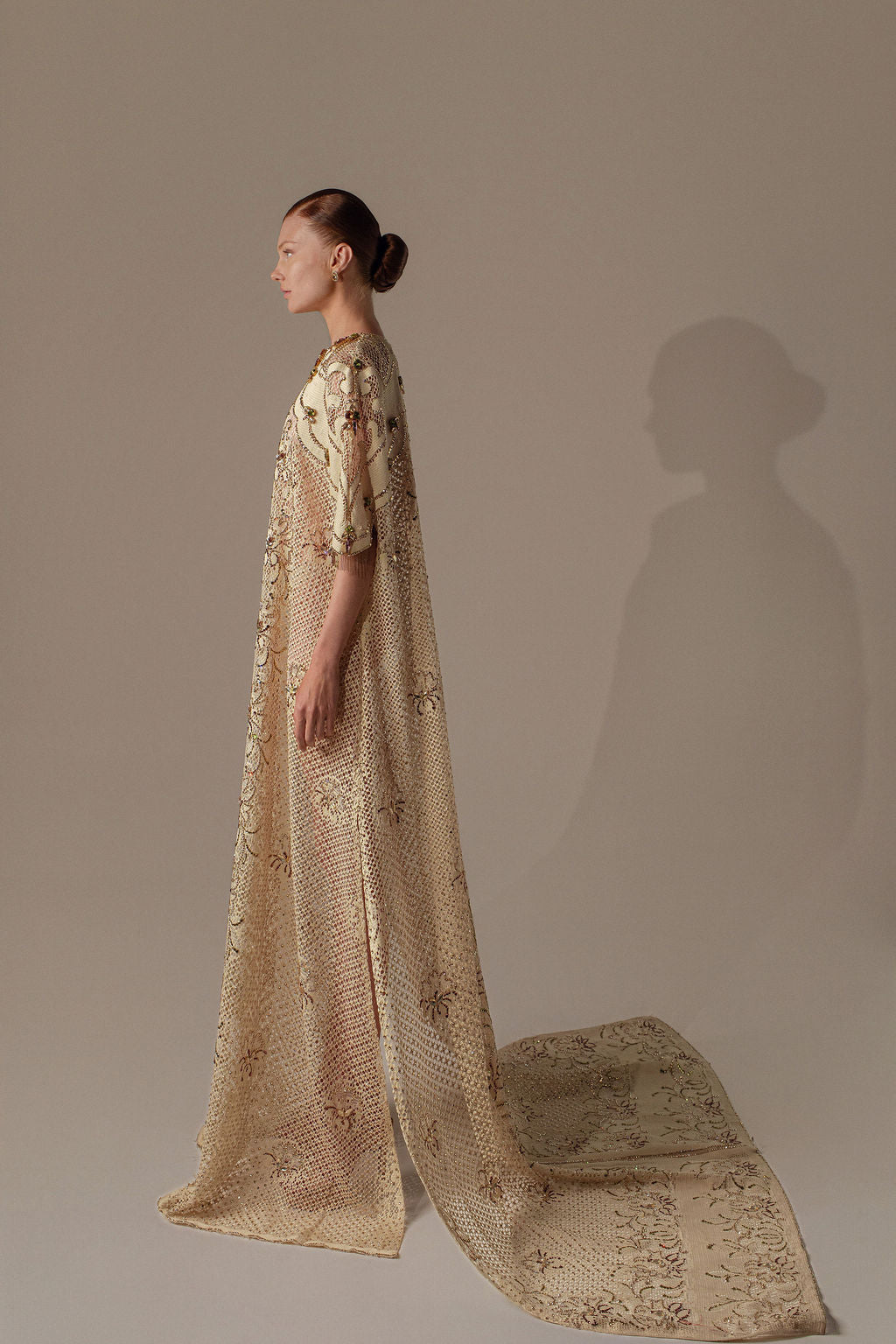 אדם בעל עור בהיר ושיער חום קצר לובש את שמלת Mira מקולקציית הערב 2026 של דרור קונטנטו — שמלת ערב מעוטרת בצבעי שמנת וזהב עם רקמת פרחים מורכבת — על רקע ניטרלי.