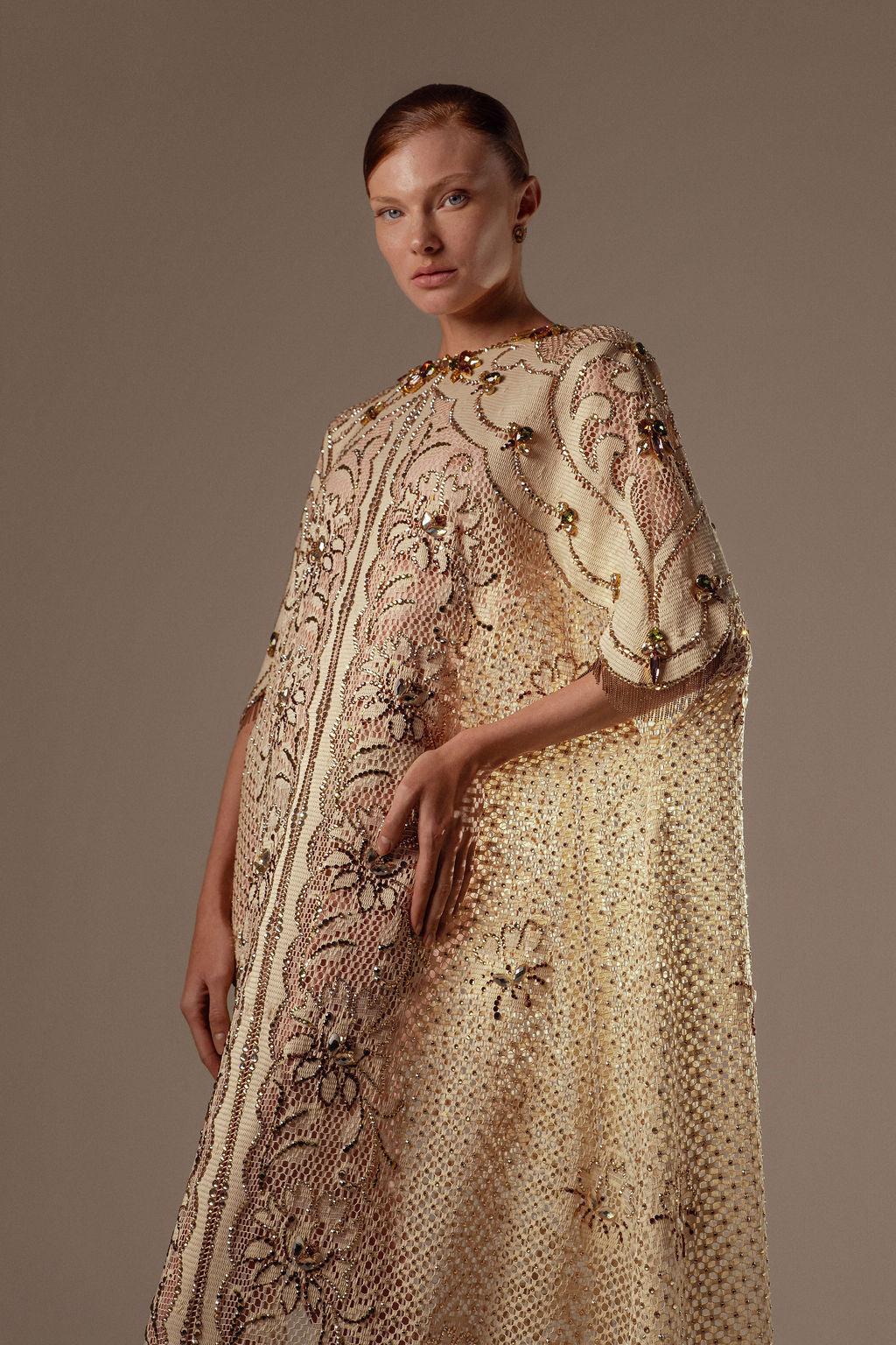 אדם בעל עור בהיר ושיער חום קצר לובש את שמלת Mira מקולקציית הערב 2026 של דרור קונטנטו — שמלת ערב מעוטרת בצבעי שמנת וזהב עם רקמת פרחים מורכבת — על רקע ניטרלי.