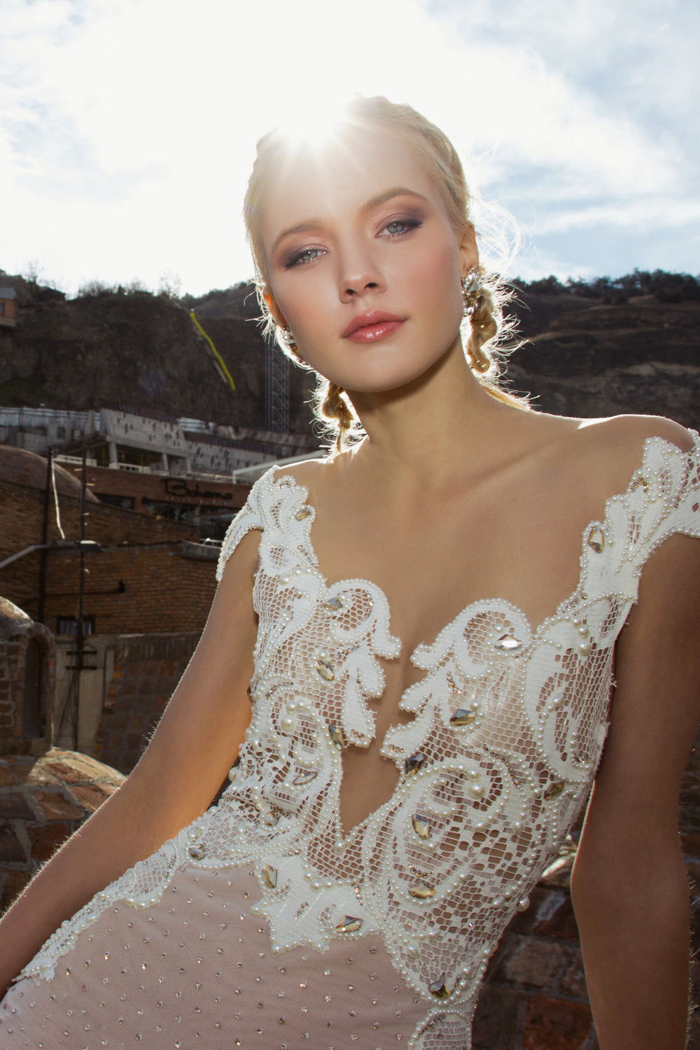 כלה לבושה בשמלת כלה בעיצוב אישי מקולקציית הכלות 2016 - 02, מצטלמת בחוץ עם אור השמש היוצר הילה מאחוריה, עומדת על רקע סלעי והררי.